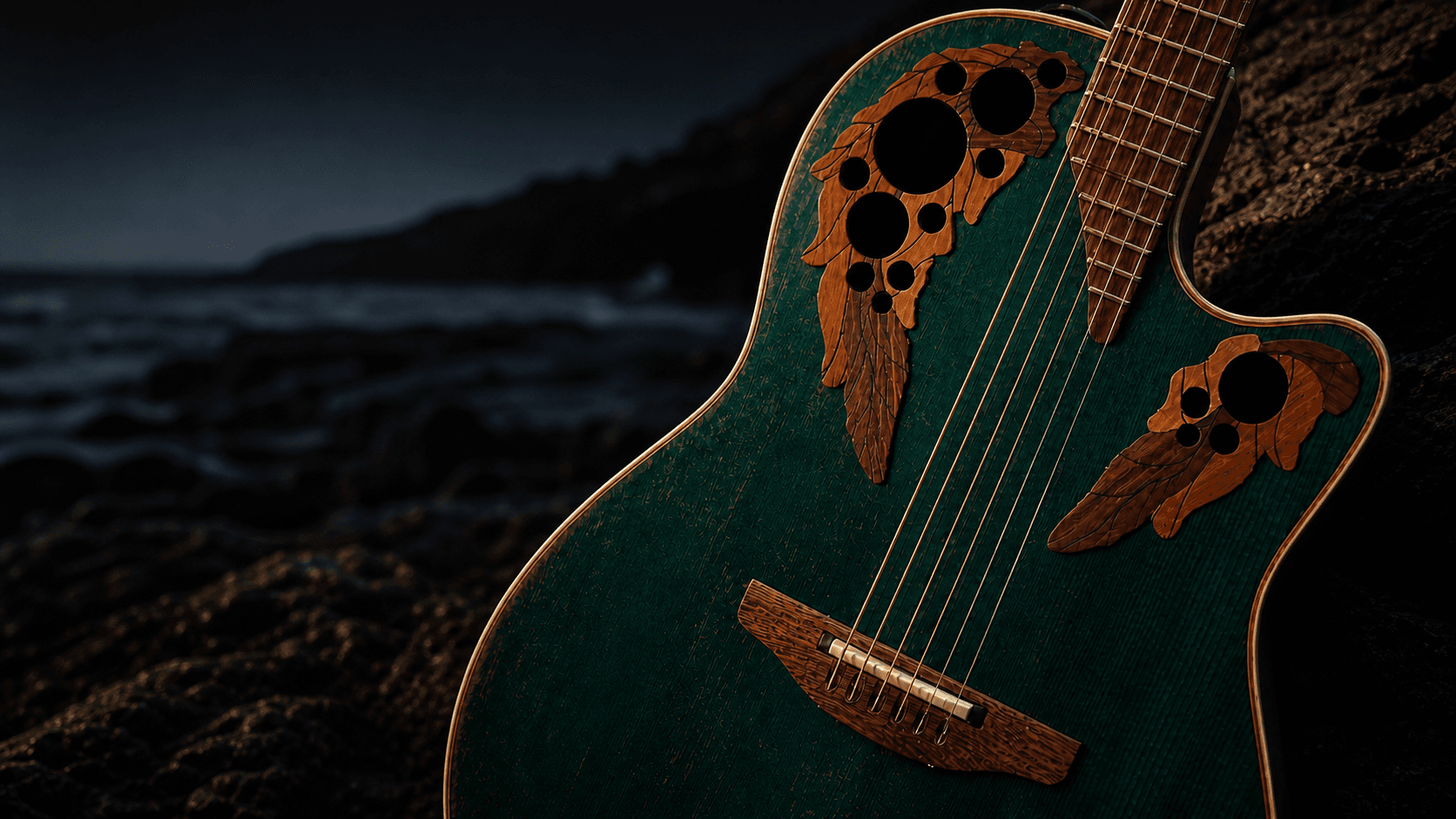 A dark teal acoustic guitar resting on shoreline rocks at dusk.